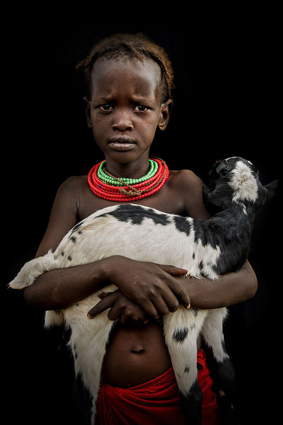 Dit meisje komt uit een Dassanech stam uit Zuid-Ethiopië en draagt een geit, hun kostbaarste bezit. De vrouwen en meisje dragen er kleurrijke hoofdbanden, kralenkettingen en armbanden. 